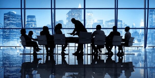 A group of people sitting at a table in front of windows.